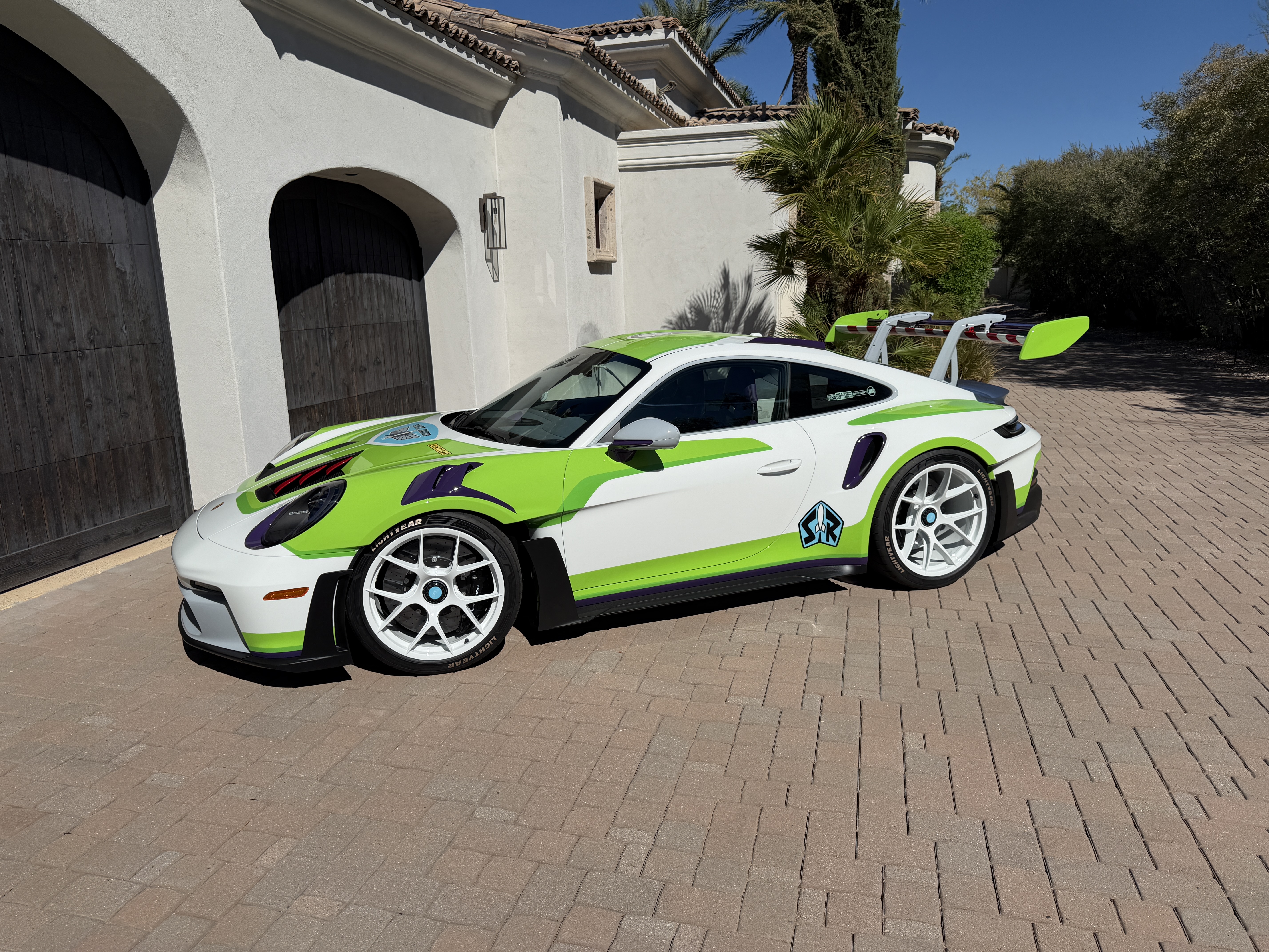 The real Buzz Lightyear Porsche 911 GT3 RS, in white, green and purple, parked in front of dark garage doors